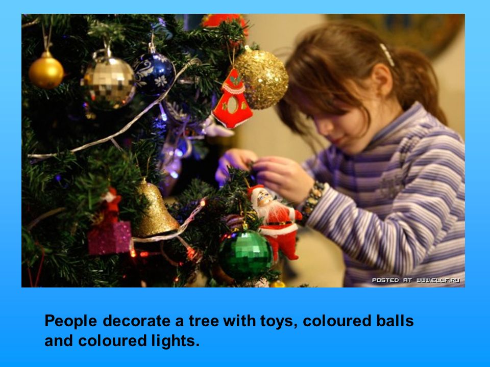 People decorate a tree with toys, coloured balls and coloured lights.